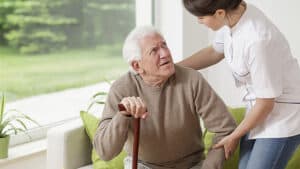 caregiver helping elderly mail patient stand