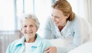 caregiver smiling behind elderly woman on couch